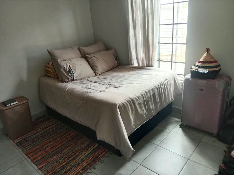 A functional bedroom featuring tiled flooring and a window fitted with security bars, providing natural light.