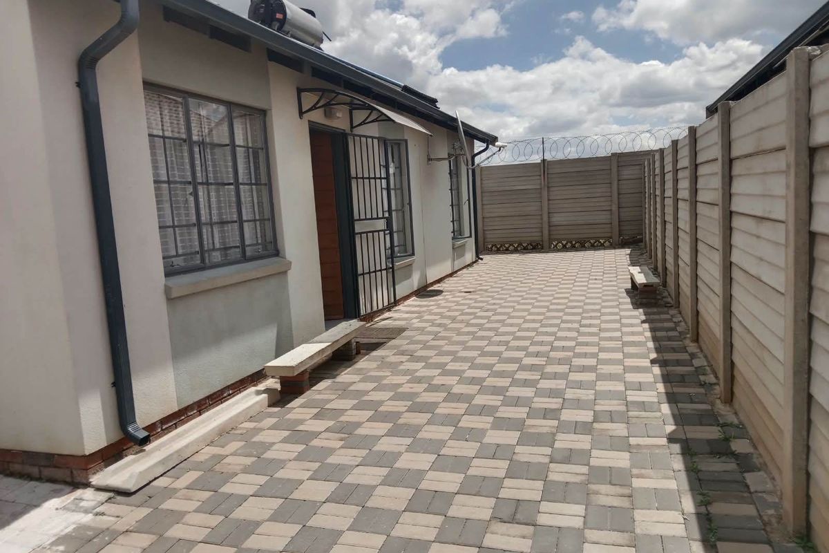 A paved rear courtyard featuring a precast concrete boundary wall with security razor wire and a solar water heater installed on the roof.