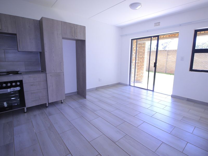 Modern open-plan kitchen and living area featuring light wood-look cabinetry, sleek tiled flooring, and direct access to an outdoor patio through sliding glass doors.
