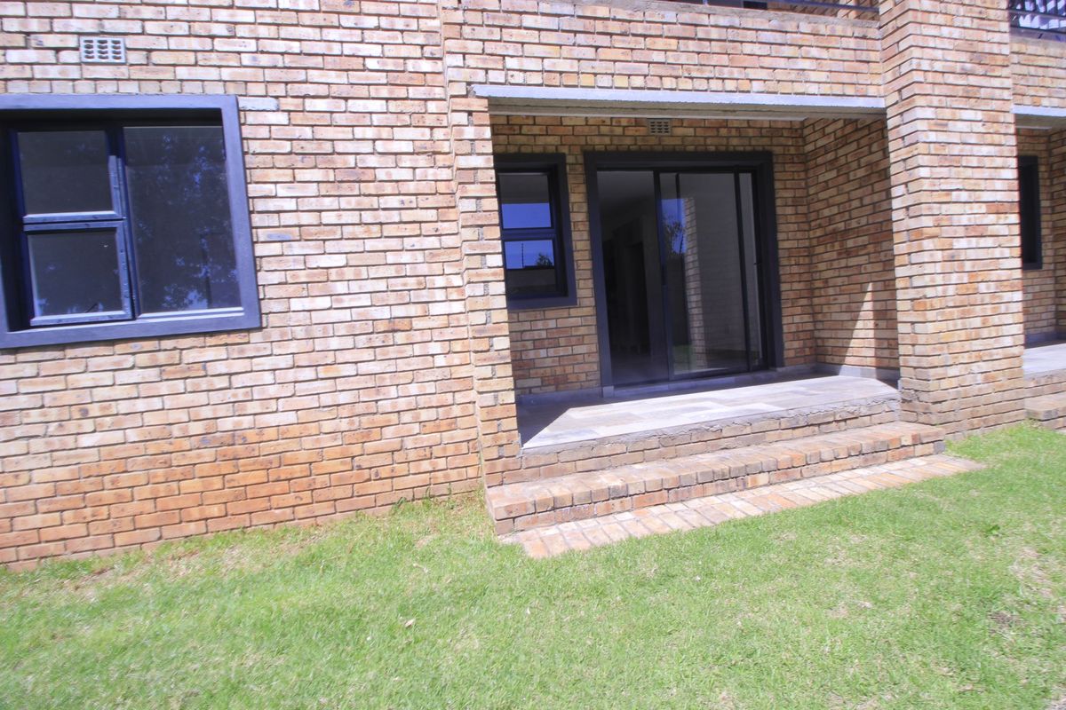 Rear exterior view of the apartment featuring a face brick facade, sliding glass door access, and a small concrete patio area leading to the garden.