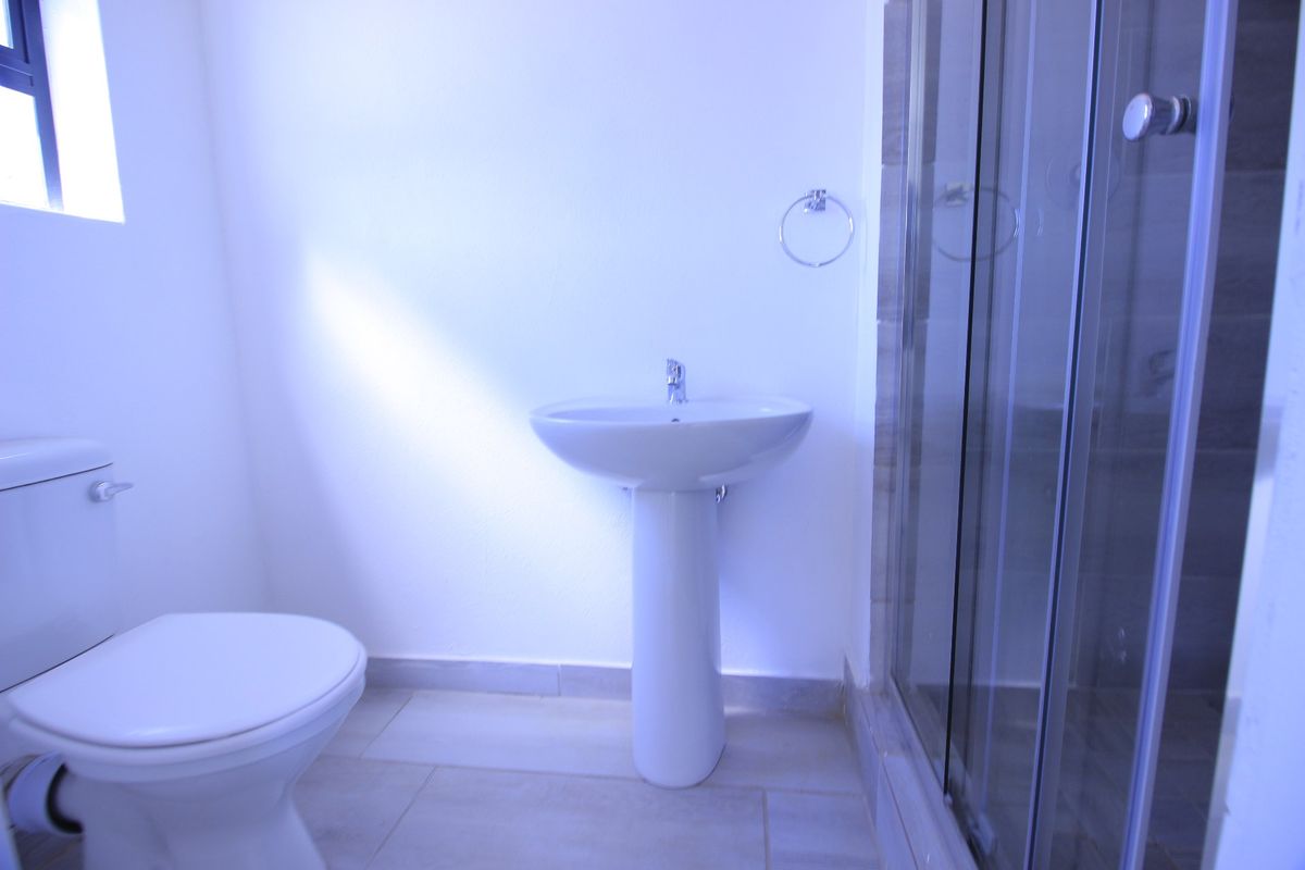 A clean and functional bathroom featuring a pedestal basin, a toilet, and a glass-enclosed shower with neutral floor tiling.