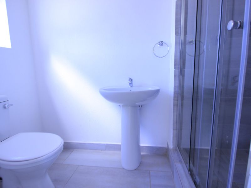 A clean and functional bathroom featuring a pedestal basin, a toilet, and a glass-enclosed shower with neutral floor tiling.