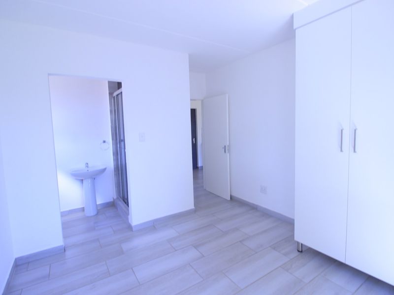 A bright, empty bedroom featuring modern tiled flooring, a built-in wardrobe, and direct access to an en-suite bathroom.