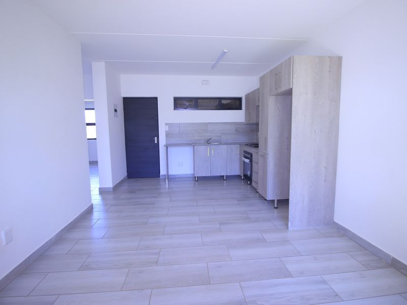 An open-plan living and kitchen area featuring modern light wood cabinetry, tiled flooring, and a neutral color palette, presenting a clean and functional space.