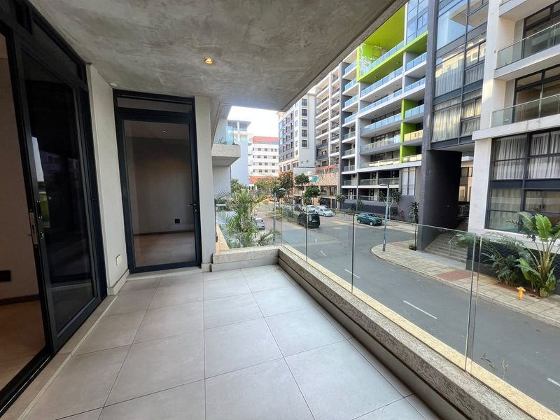 A modern, spacious balcony featuring tiled flooring, a sleek glass balustrade, and recessed lighting, offering an elevated view of the surrounding urban streetscape.