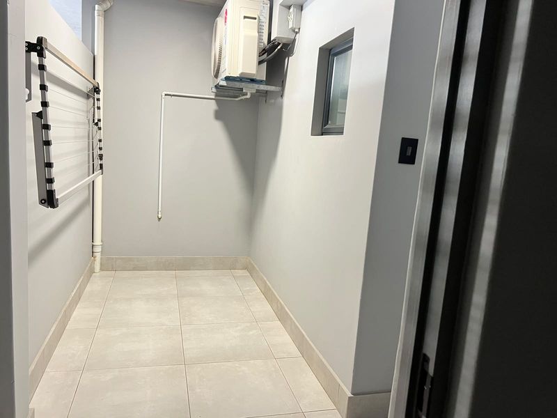 A clean and functional utility space featuring tiled flooring, a wall-mounted drying rack, and an installed air conditioning condenser unit.