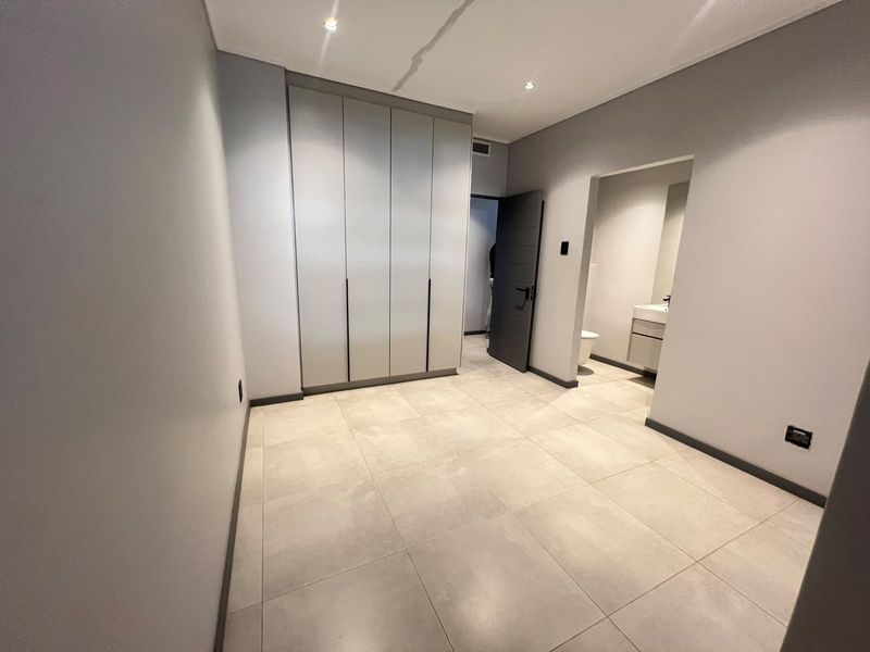 A modern, empty bedroom featuring neutral tiled flooring, built-in cupboards, and direct access to an en-suite bathroom.