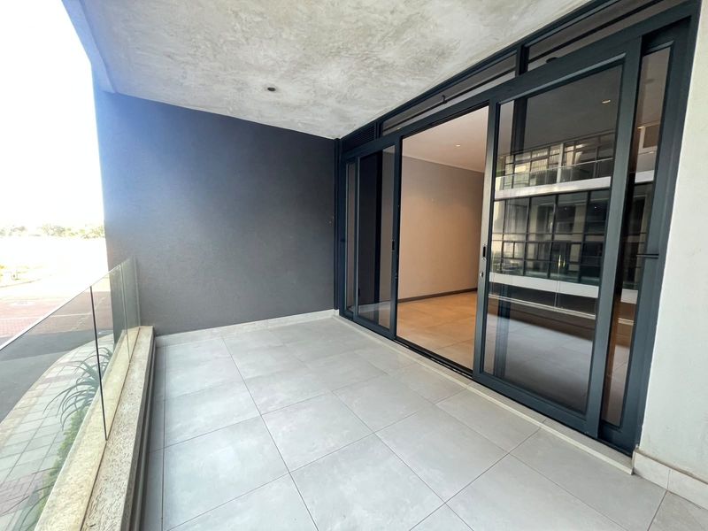 Modern covered balcony featuring large sliding glass doors, sleek tiled flooring, and a contemporary glass balustrade overlooking the surrounding area.