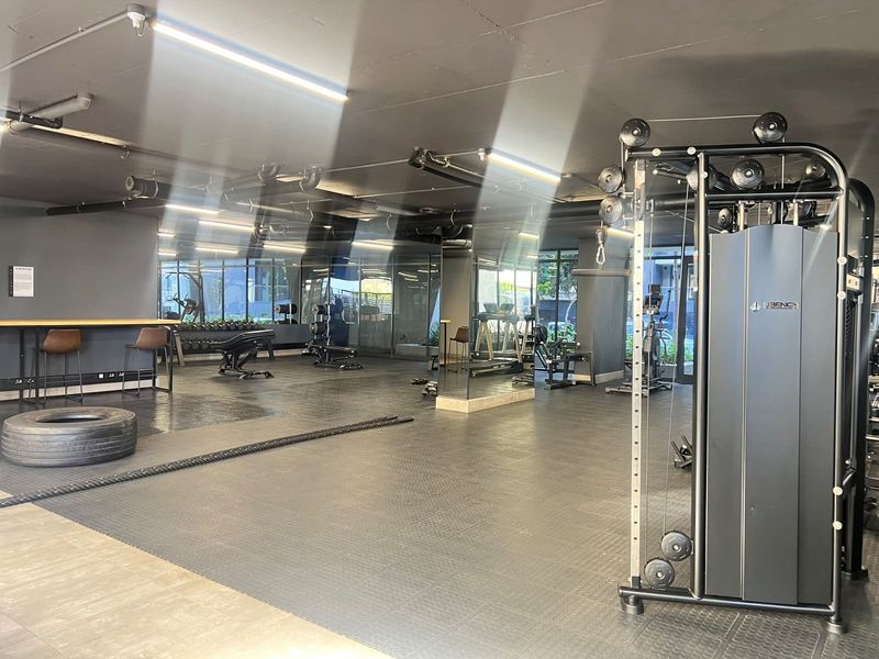A modern, well-equipped apartment gym featuring rubber flooring, mirrored walls, and an industrial-style exposed ceiling with integrated lighting.
