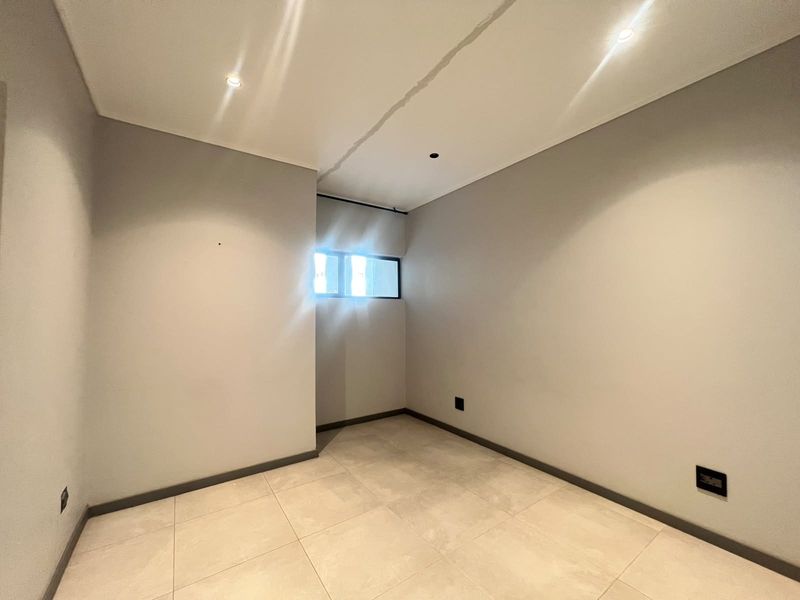 An empty bedroom featuring neutral tiled flooring, recessed ceiling lighting, and a small window, providing a blank canvas for personalization.