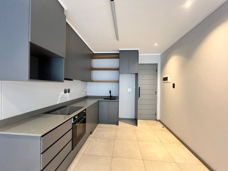 Modern kitchen featuring sleek grey cabinetry, stone countertops, integrated oven, electric hob, and open shelving, finished with neutral floor tiles.