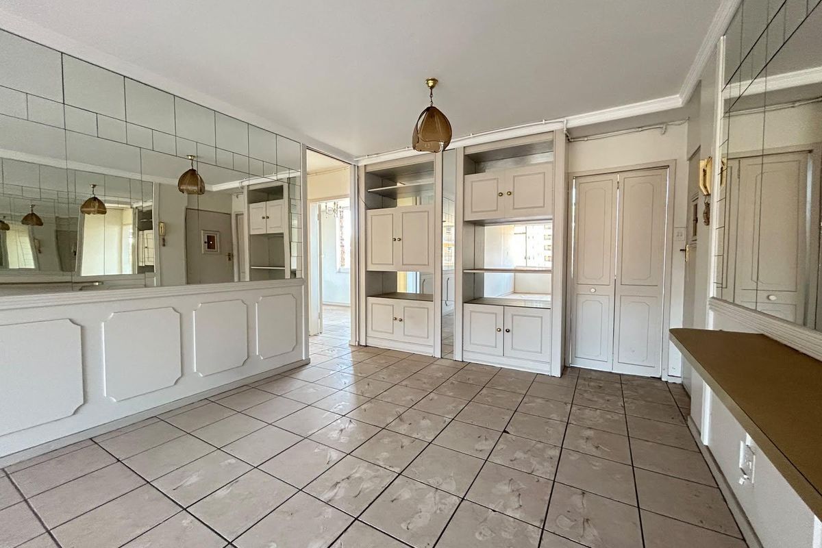 An empty living area featuring tiled flooring, extensive built-in cabinetry, and mirrored wall panels, offering a blank canvas for renovation and modernization.