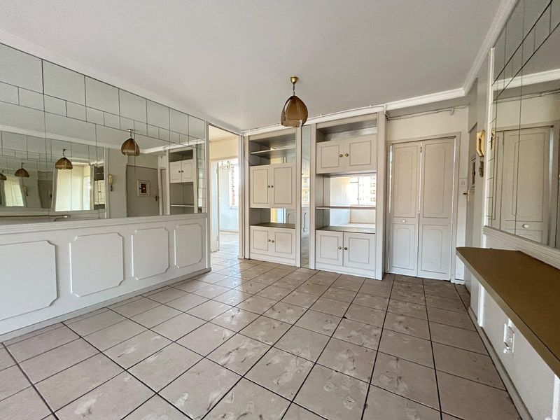 An empty living area featuring tiled flooring, extensive built-in cabinetry, and mirrored wall panels, offering a blank canvas for renovation and modernization.