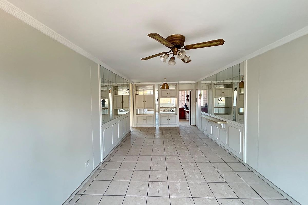 Spacious living area featuring tiled flooring, ceiling fan, and extensive built-in mirrored cabinetry, offering a versatile layout ready for modern updates.