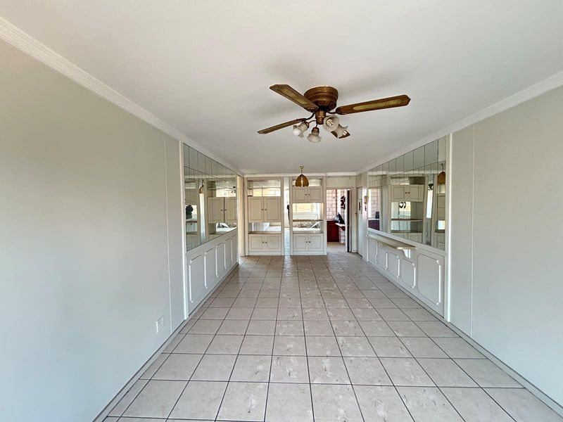 Spacious living area featuring tiled flooring, ceiling fan, and extensive built-in mirrored cabinetry, offering a versatile layout ready for modern updates.
