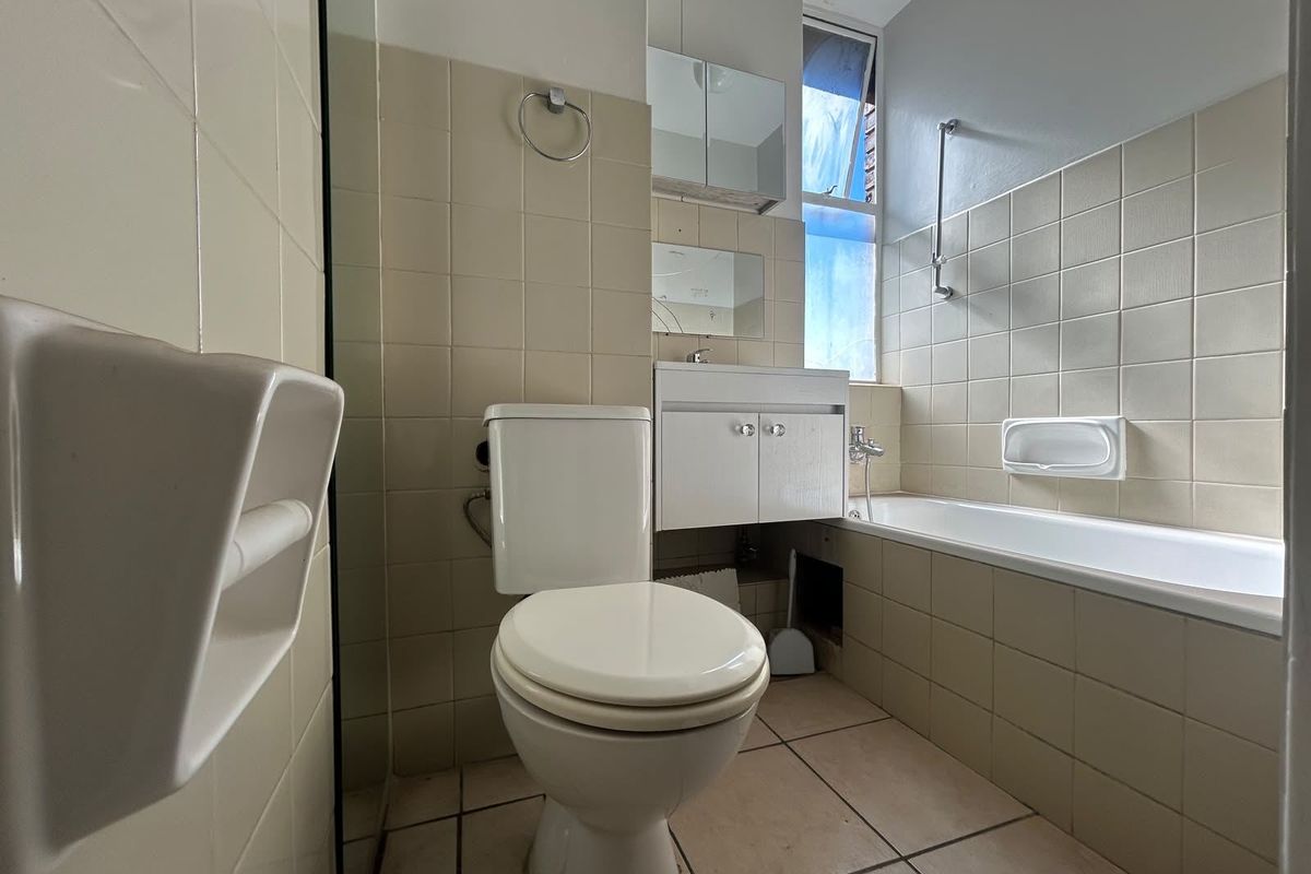 A functional bathroom featuring a bathtub, toilet, and vanity cabinet with tiled finishes, offering a blank canvas for potential modernization and renovation.