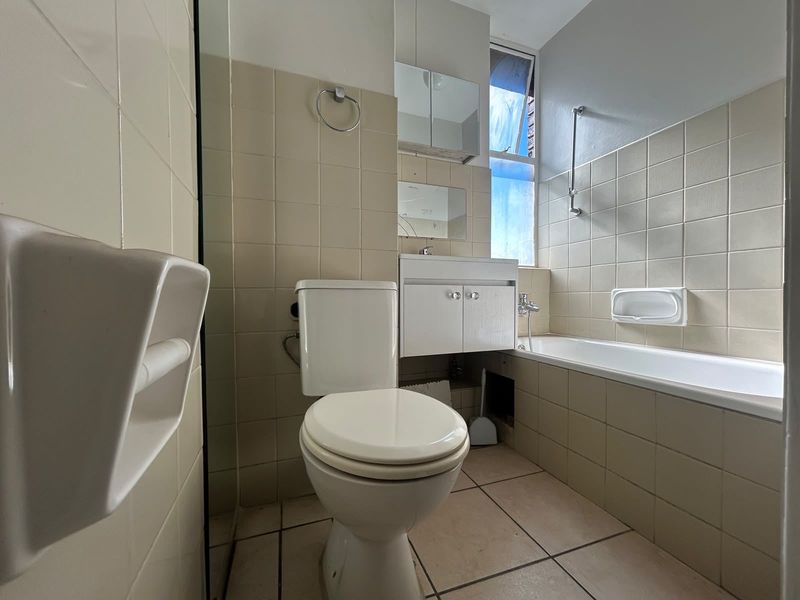 A functional bathroom featuring a bathtub, toilet, and vanity cabinet with tiled finishes, offering a blank canvas for potential modernization and renovation.