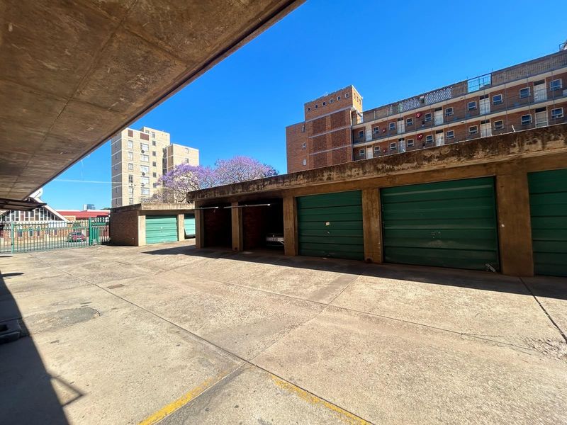 A view of a communal parking area featuring multiple garage units with metal doors and a concrete driveway.
