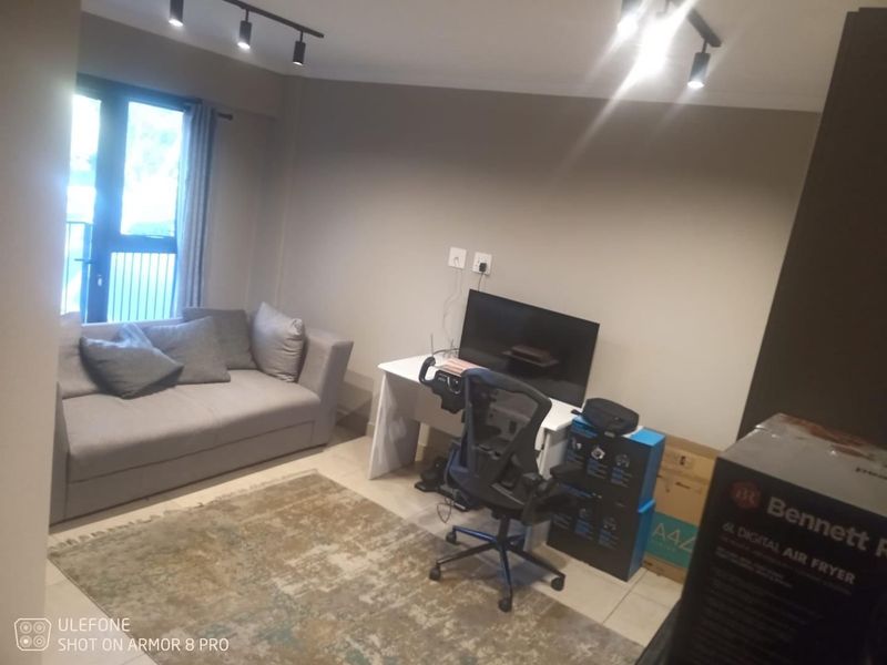 A living room area featuring tiled flooring, track lighting, and a sliding door leading to a balcony.