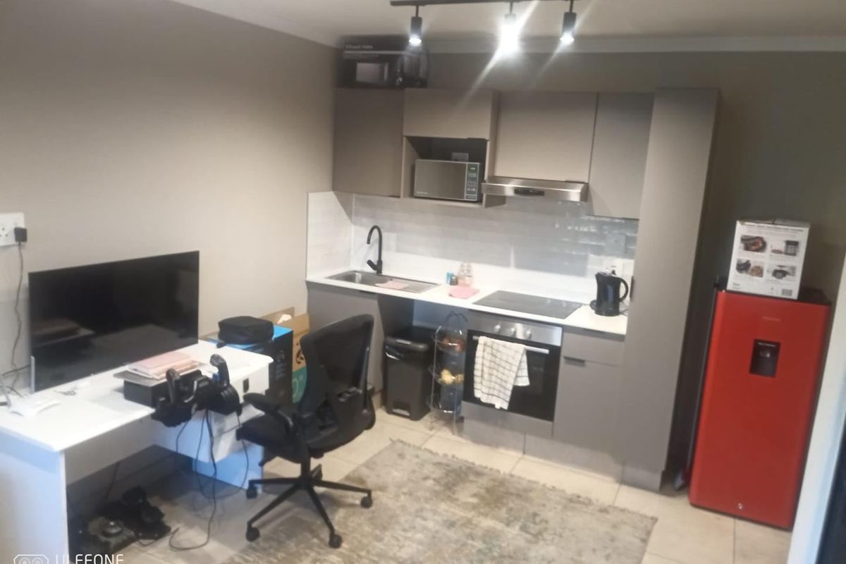 Compact open-plan kitchen area featuring modern grey cabinetry, integrated appliances, and a tiled backsplash, seamlessly connected to a functional living or workspace.