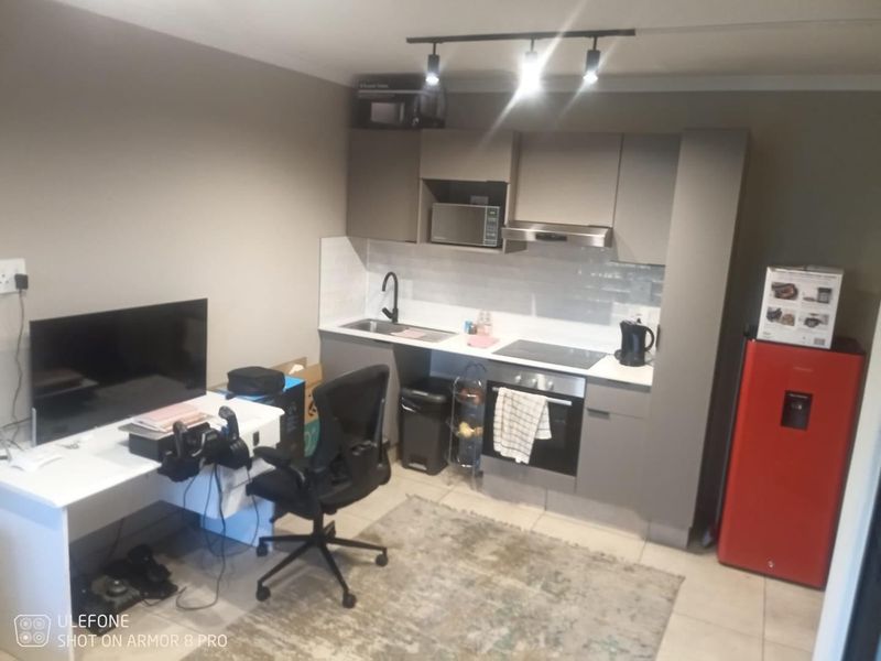Compact open-plan kitchen area featuring modern grey cabinetry, integrated appliances, and a tiled backsplash, seamlessly connected to a functional living or workspace.
