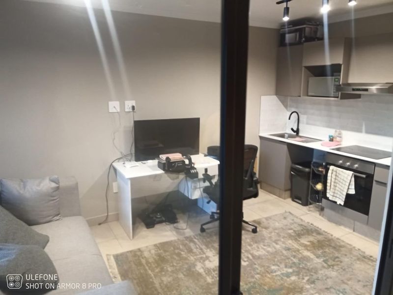 Compact open-plan living area featuring a modern kitchen with built-in cabinetry, electric hob, oven, and tiled flooring.