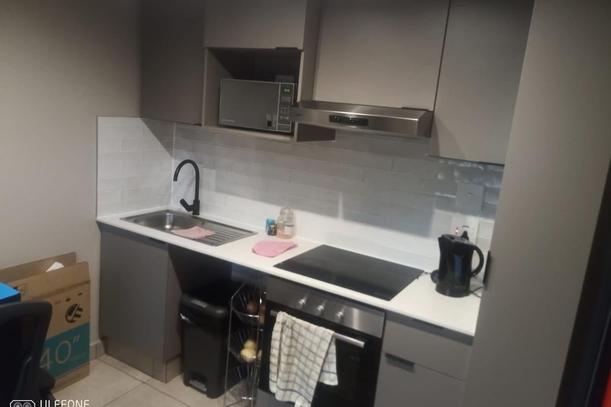 Compact modern kitchen featuring sleek grey cabinetry, white countertops, subway tile backsplash, and integrated stainless steel appliances including an oven and extractor fan.