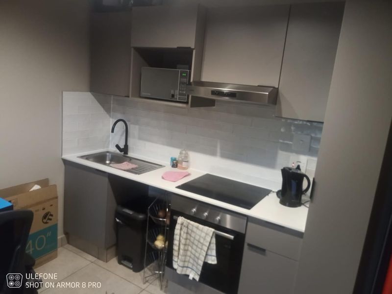Compact modern kitchen featuring sleek grey cabinetry, white countertops, subway tile backsplash, and integrated stainless steel appliances including an oven and extractor fan.