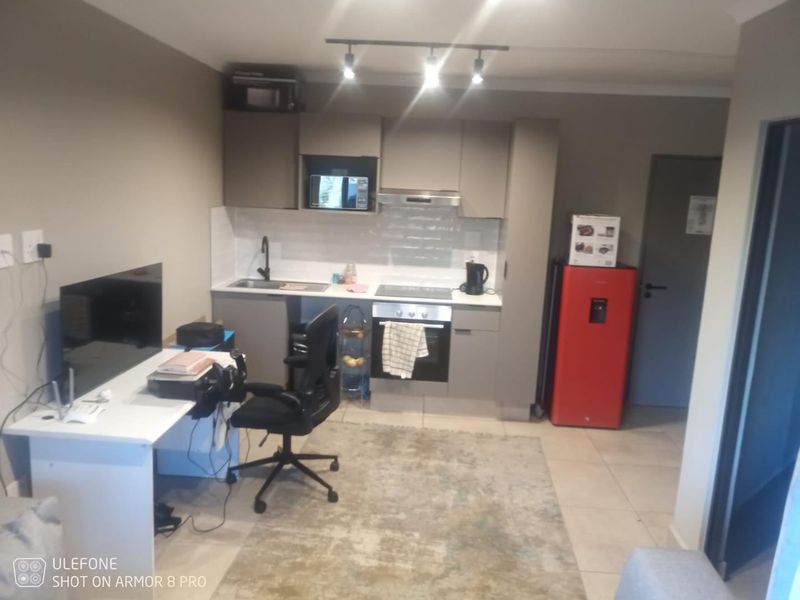 Compact open-plan kitchen area featuring modern grey cabinetry, integrated appliances, and tiled flooring, seamlessly connected to the living space.