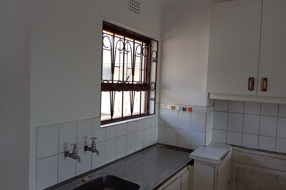 A functional kitchen area featuring a stainless steel sink, tiled splashback, and built-in cabinetry, ready for modernization and cosmetic updates.