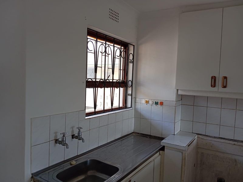 A functional kitchen area featuring a stainless steel sink, tiled splashback, and built-in cabinetry, ready for modernization and cosmetic updates.