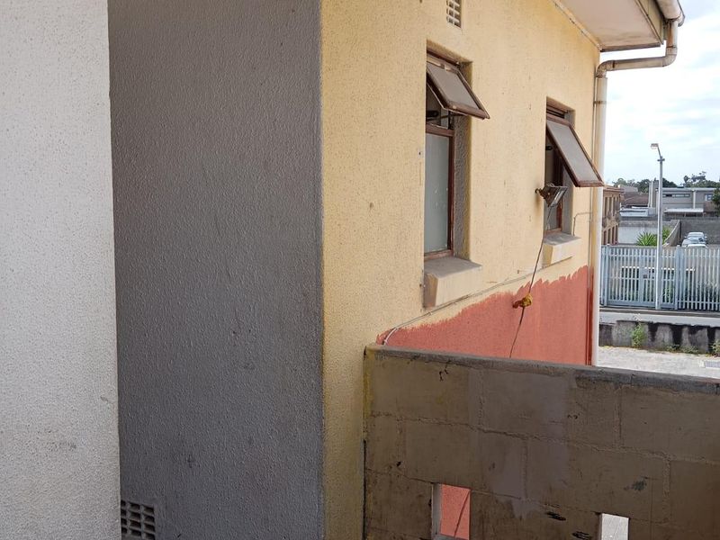 An exterior balcony area featuring a concrete block balustrade and weathered exterior wall finishes, requiring maintenance and cosmetic updates.