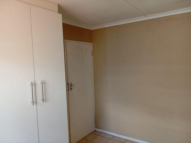 A vacant bedroom featuring built-in cupboards and tiled flooring, requiring minor cosmetic updates to the wall finishes.