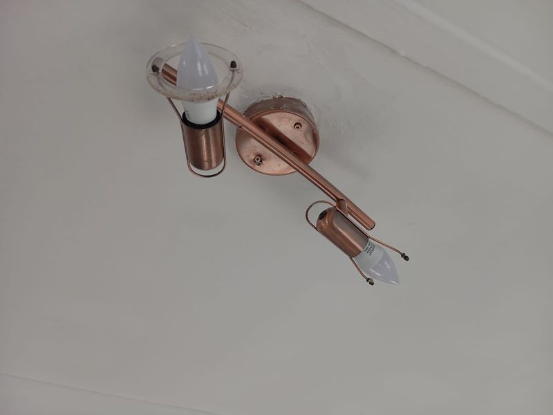 A close-up view of a copper-finish dual spotlight fixture mounted on a white ceiling.