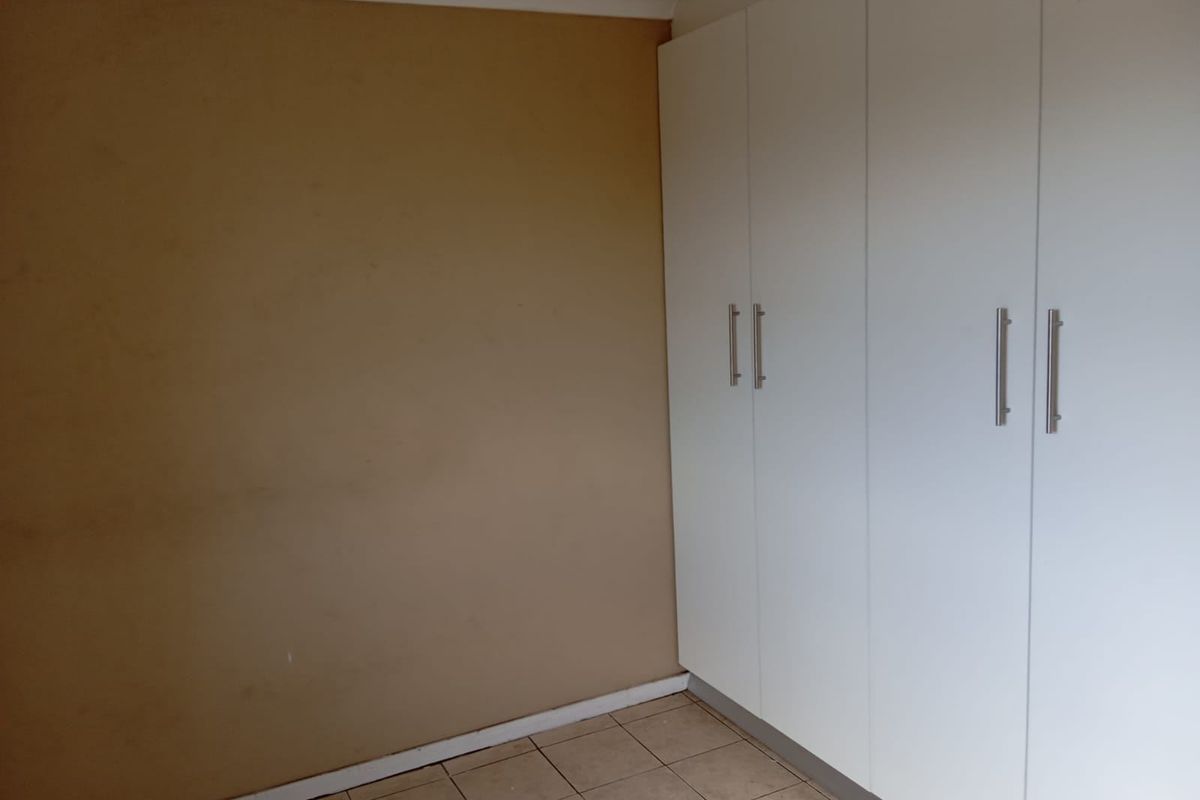 A bedroom featuring tiled flooring and white built-in cupboards, providing ample storage space. The room is currently empty and ready for personalization.
