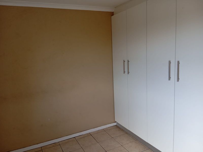 A bedroom featuring tiled flooring and white built-in cupboards, providing ample storage space. The room is currently empty and ready for personalization.