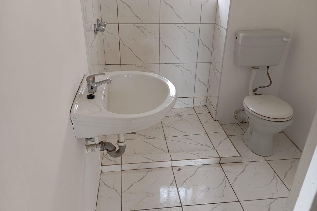 A compact bathroom featuring a wall-mounted basin and toilet with tiled flooring and wall finishes.