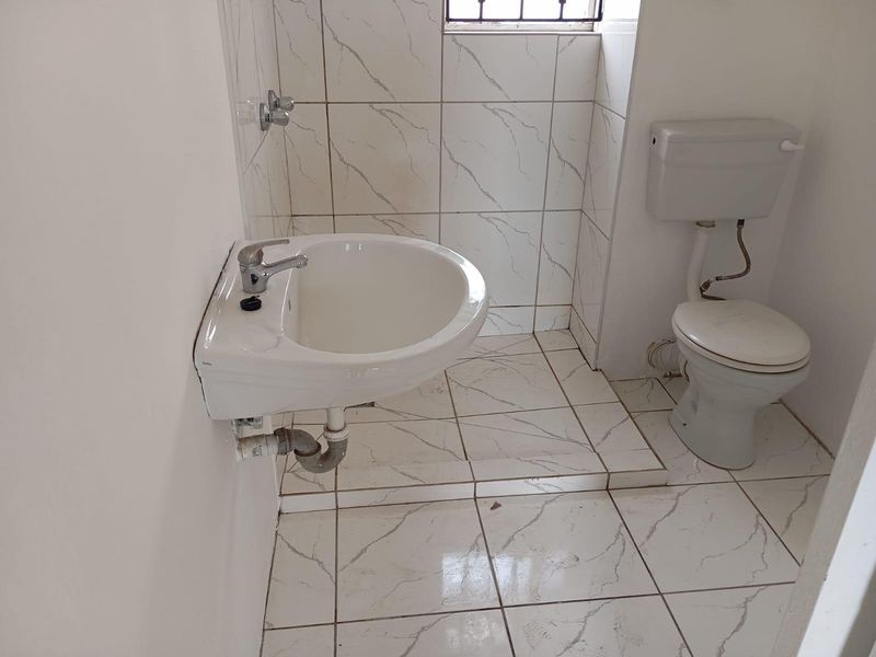 A compact bathroom featuring a wall-mounted basin and toilet with tiled flooring and wall finishes.