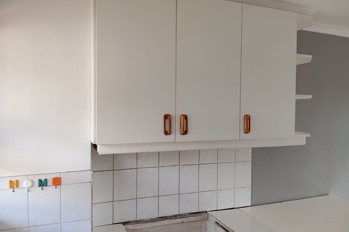 A kitchen area featuring white wall-mounted cabinetry, a tiled backsplash, and open shelving, currently awaiting the installation of a sink or cooktop.