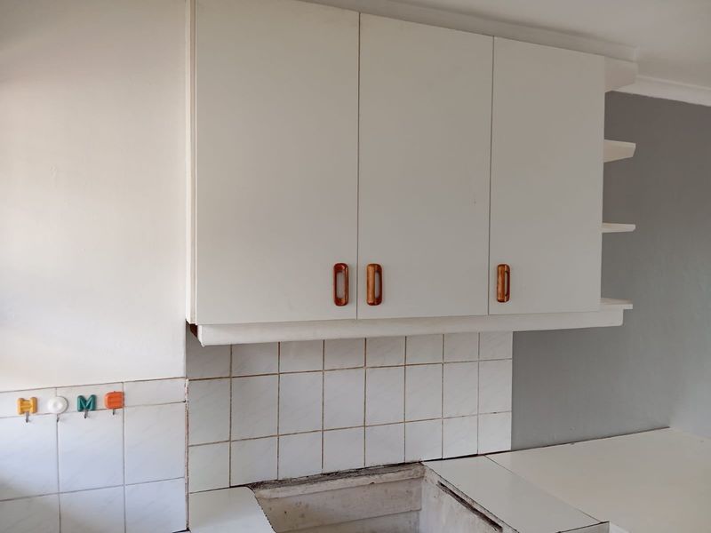A kitchen area featuring white wall-mounted cabinetry, a tiled backsplash, and open shelving, currently awaiting the installation of a sink or cooktop.