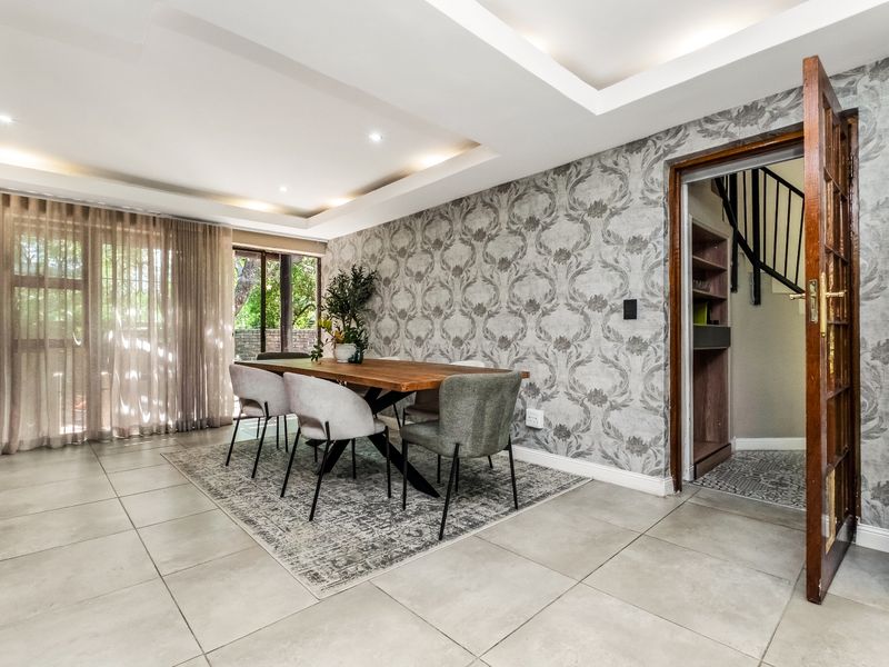 A well-lit dining room featuring tiled floors, a decorative wallpaper feature wall, recessed ceiling lighting, and direct access to a staircase area.