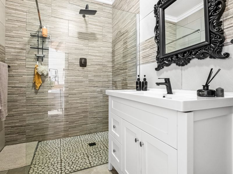 Modern bathroom featuring a walk-in shower with pebble flooring, a sleek white vanity with a black mixer tap, and contemporary wall tiling.