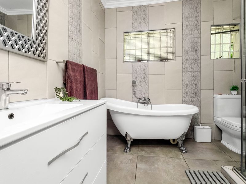 Modern bathroom featuring a classic freestanding clawfoot bathtub, a sleek vanity unit, a separate shower enclosure, and neutral floor-to-ceiling wall tiling.