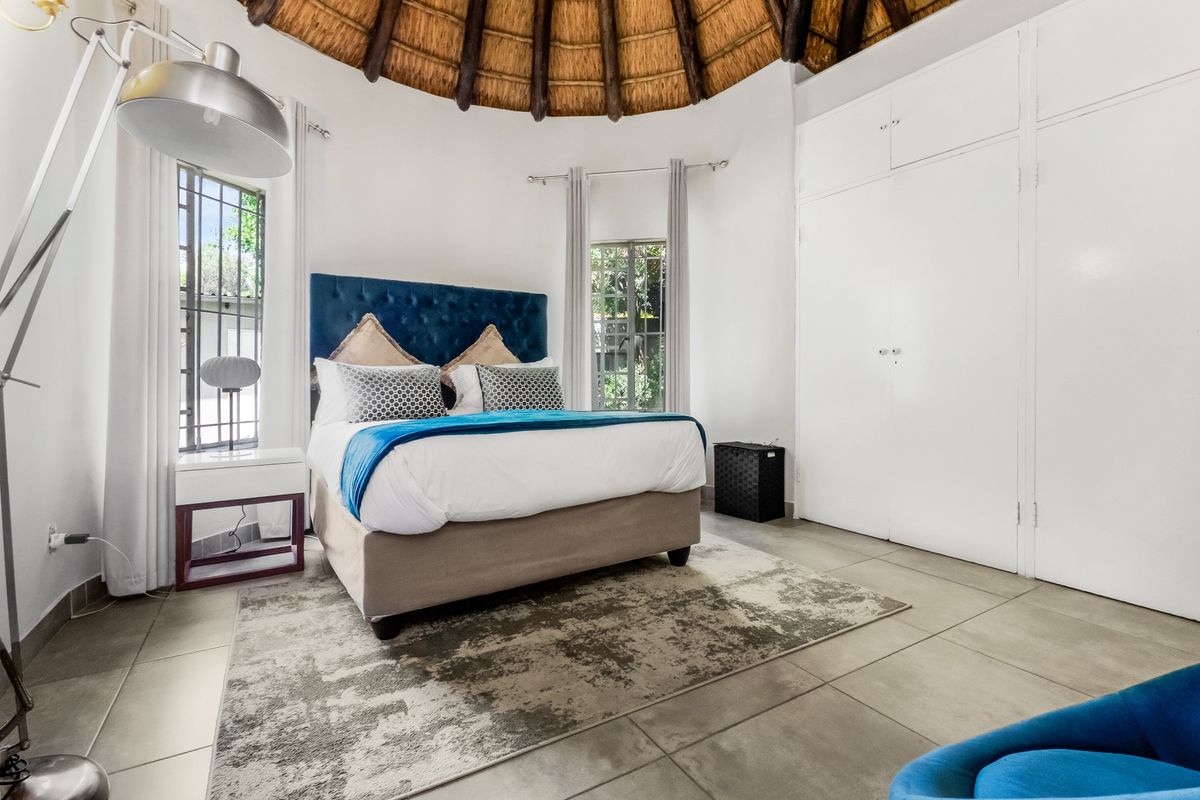 A spacious bedroom featuring a unique circular thatched roof, tiled flooring, and ample built-in cupboard storage.
