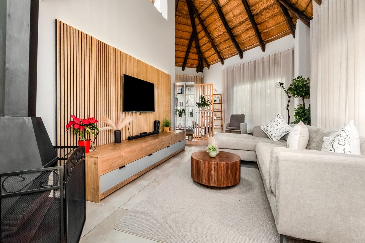 Spacious living room featuring a high vaulted thatched ceiling with exposed timber rafters, a modern wood slat feature wall, and a cozy fireplace.