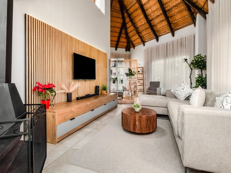 Spacious living room featuring a high vaulted thatched ceiling with exposed timber rafters, a modern wood slat feature wall, and a cozy fireplace.