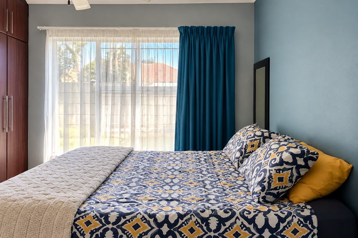 A well-maintained bedroom featuring built-in cupboards, a ceiling fan, and a large window that allows for natural light.