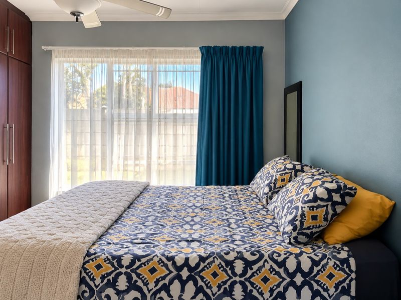A well-maintained bedroom featuring built-in cupboards, a ceiling fan, and a large window that allows for natural light.