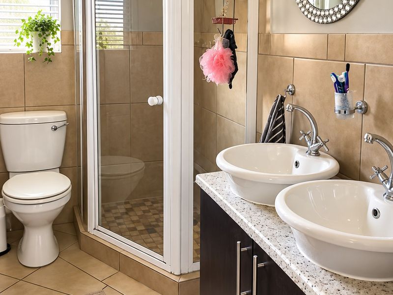 A functional bathroom featuring a double vanity with vessel sinks, a corner shower enclosure, and neutral tiled finishes throughout.