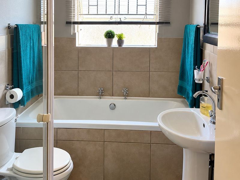 A clean and functional bathroom featuring a built-in bathtub, pedestal basin, toilet, and a separate shower enclosure with neutral wall and floor tiling.